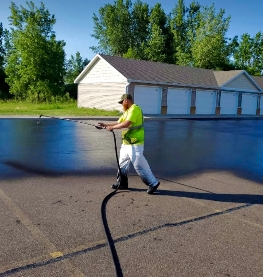 South Texas Asphalt Maintenance crew member spray-applying sealcoat to a driveway